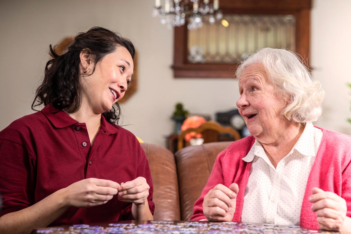 Aging woman and Care Professional work on puzzle together at home