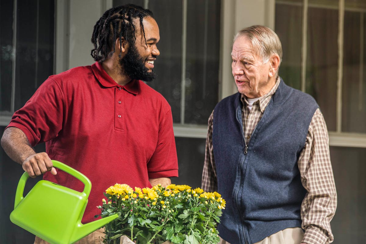 Care Professional and aging man water flowers outside