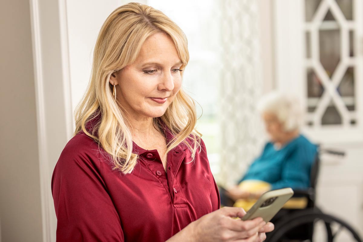 Care Professional reviews mobile app with senior woman sitting in background