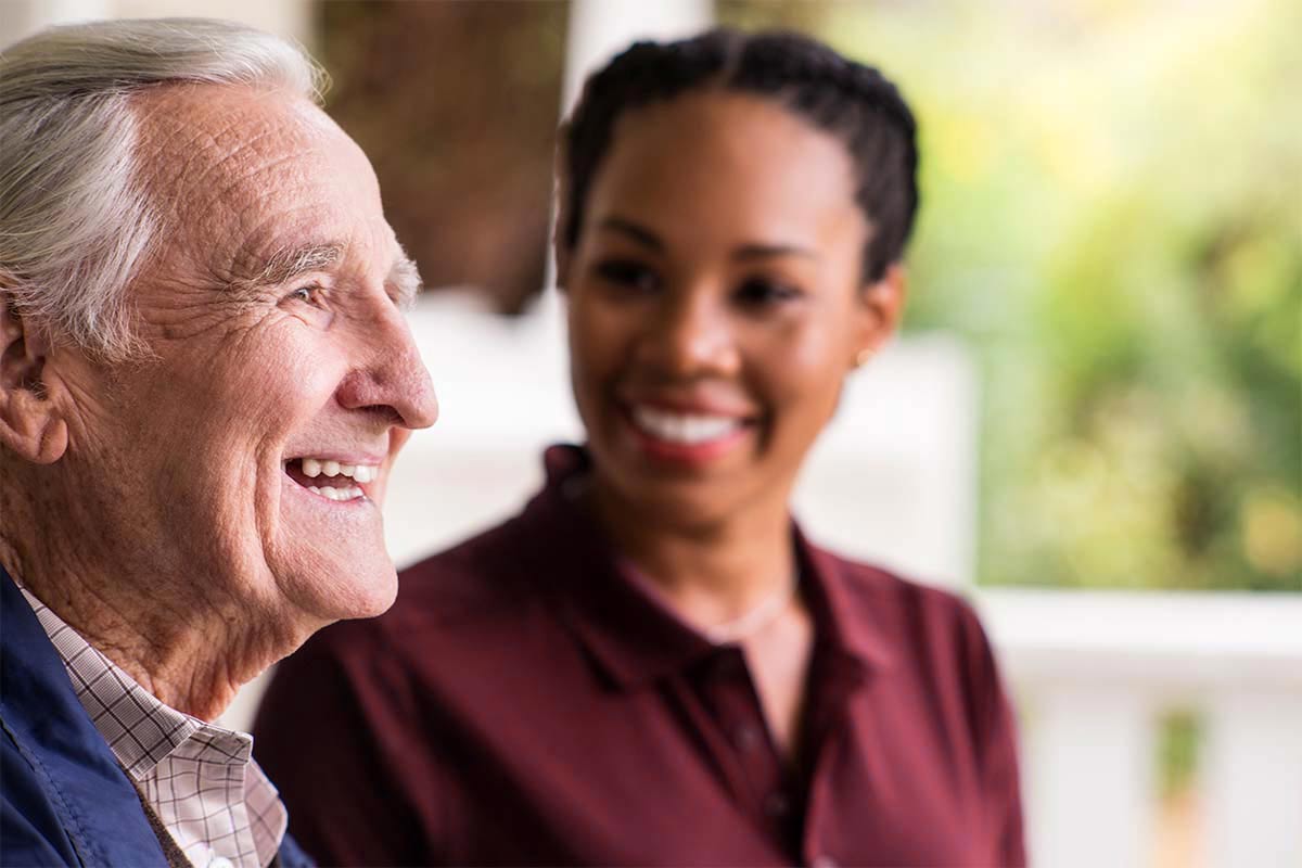 Senior man laughs with Care Professional in background