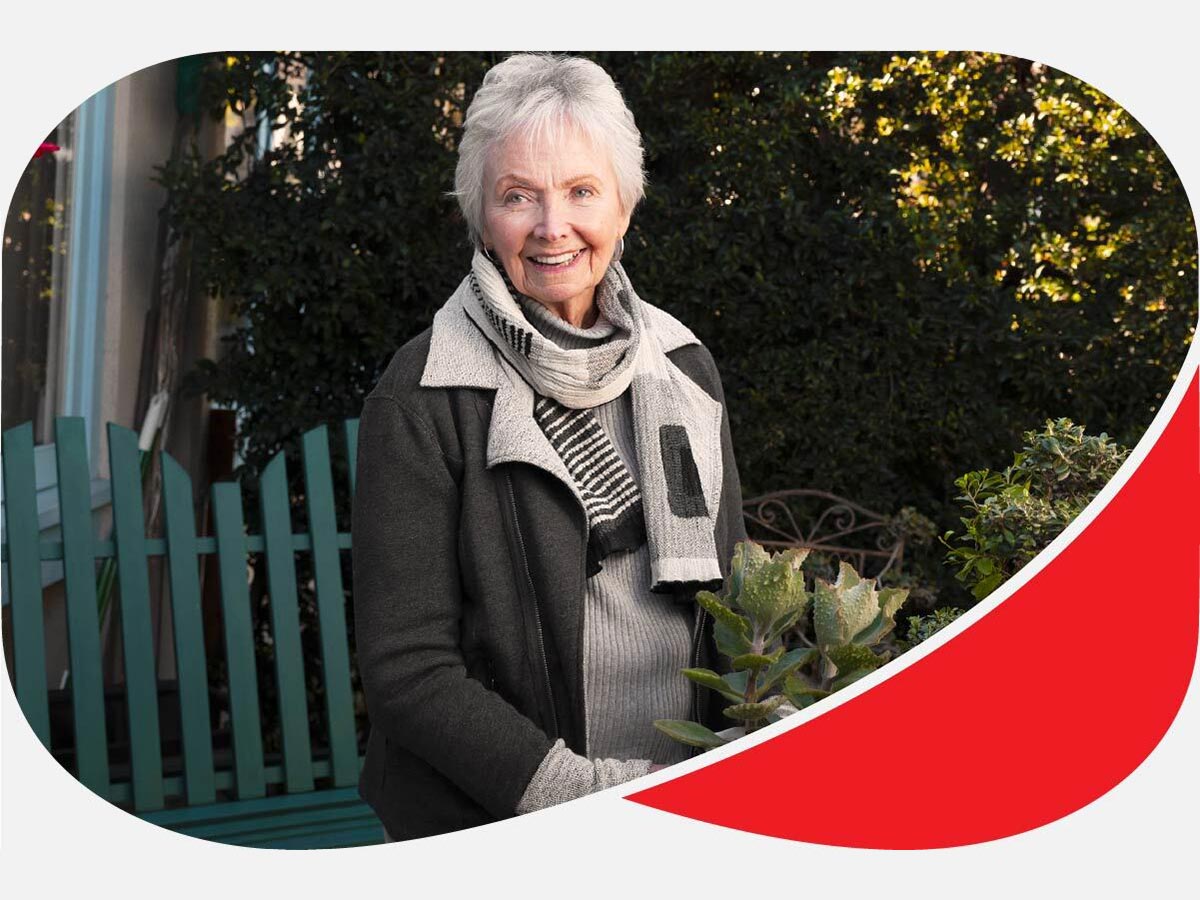 Senior woman smiles and holds potted plant in garden